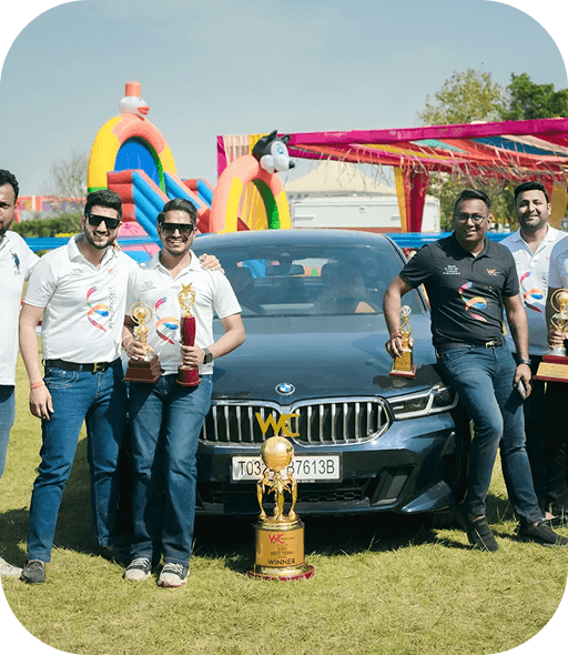 Team members posing with trophies beside a car at a company event